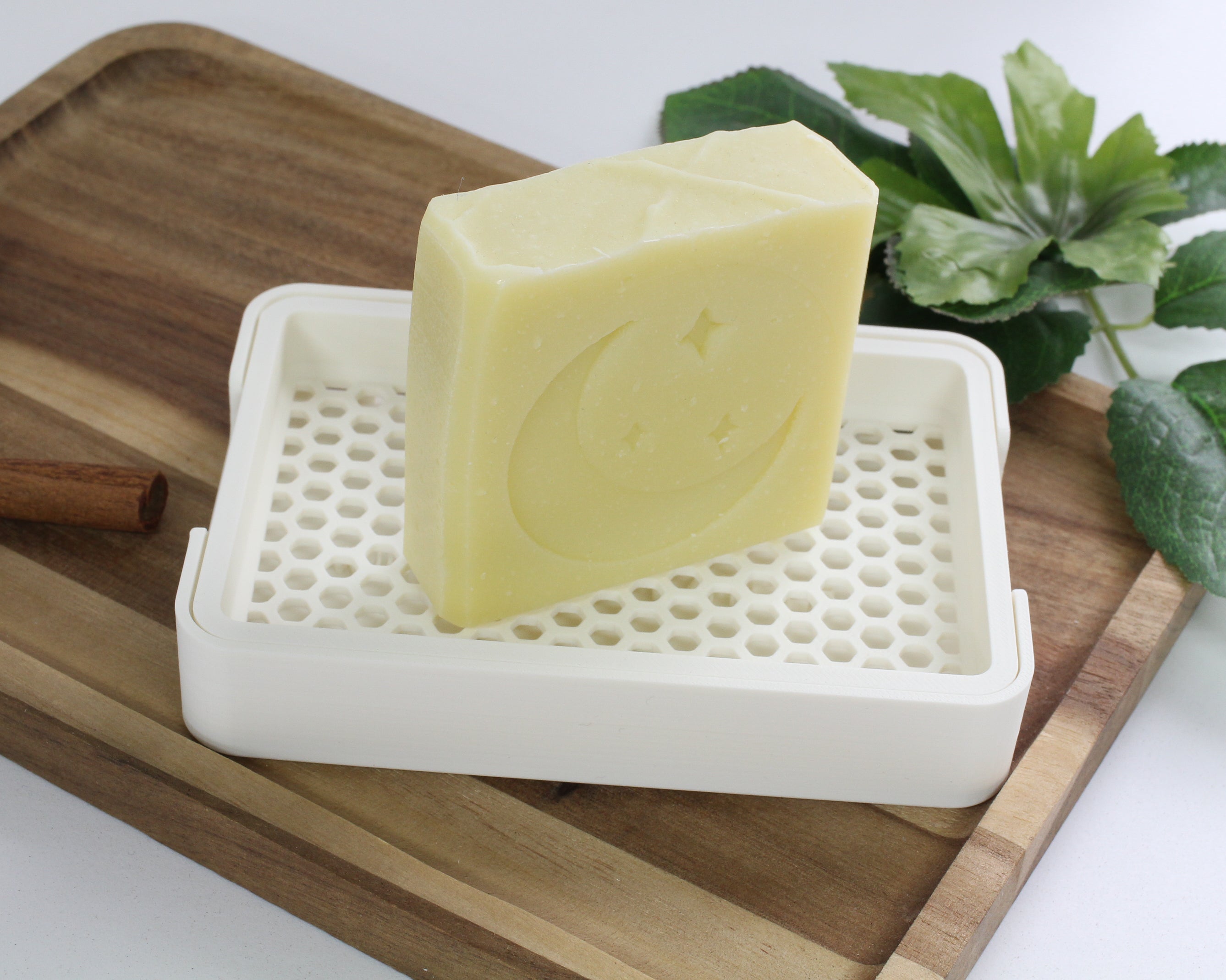 Bar of soap on a white soap dish with a wooden tray and green plant in the background